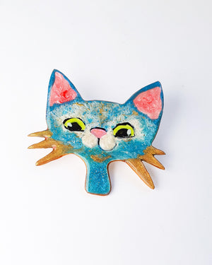 A blue white and gold cat brooch on a white background.  This kitty pin has gold whiskers, big green eyes and a pink nose. She's full of sparkle.