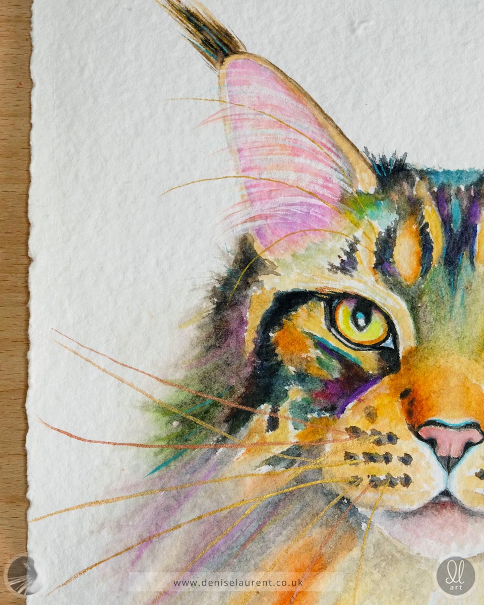 Close up of a watercolor painting of a tabby cat's face on handmade paper showing her gold and copper whiskers, her ear tufts and details of the deckled paper edges.