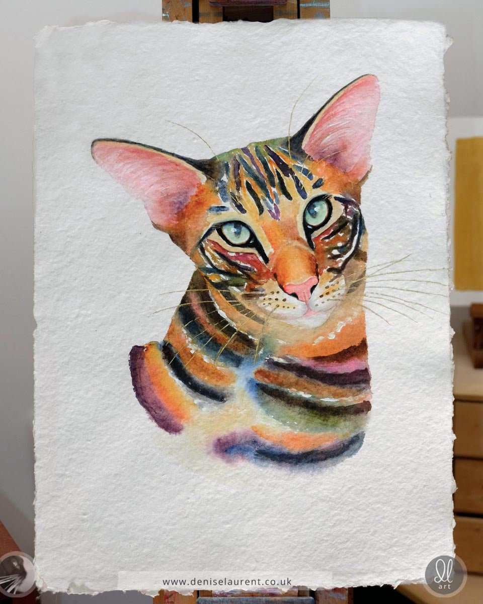 Colorful watercolor painting of a brown tabby cat on handmade paper, on the artists easel.