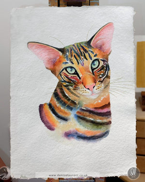 Colorful watercolor painting of a brown tabby cat on handmade paper, on the artists easel.