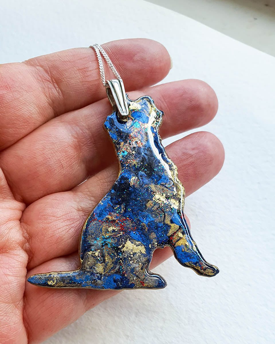 Border terrier dog shaped Blue and gold  pendant held in a hand against a white background