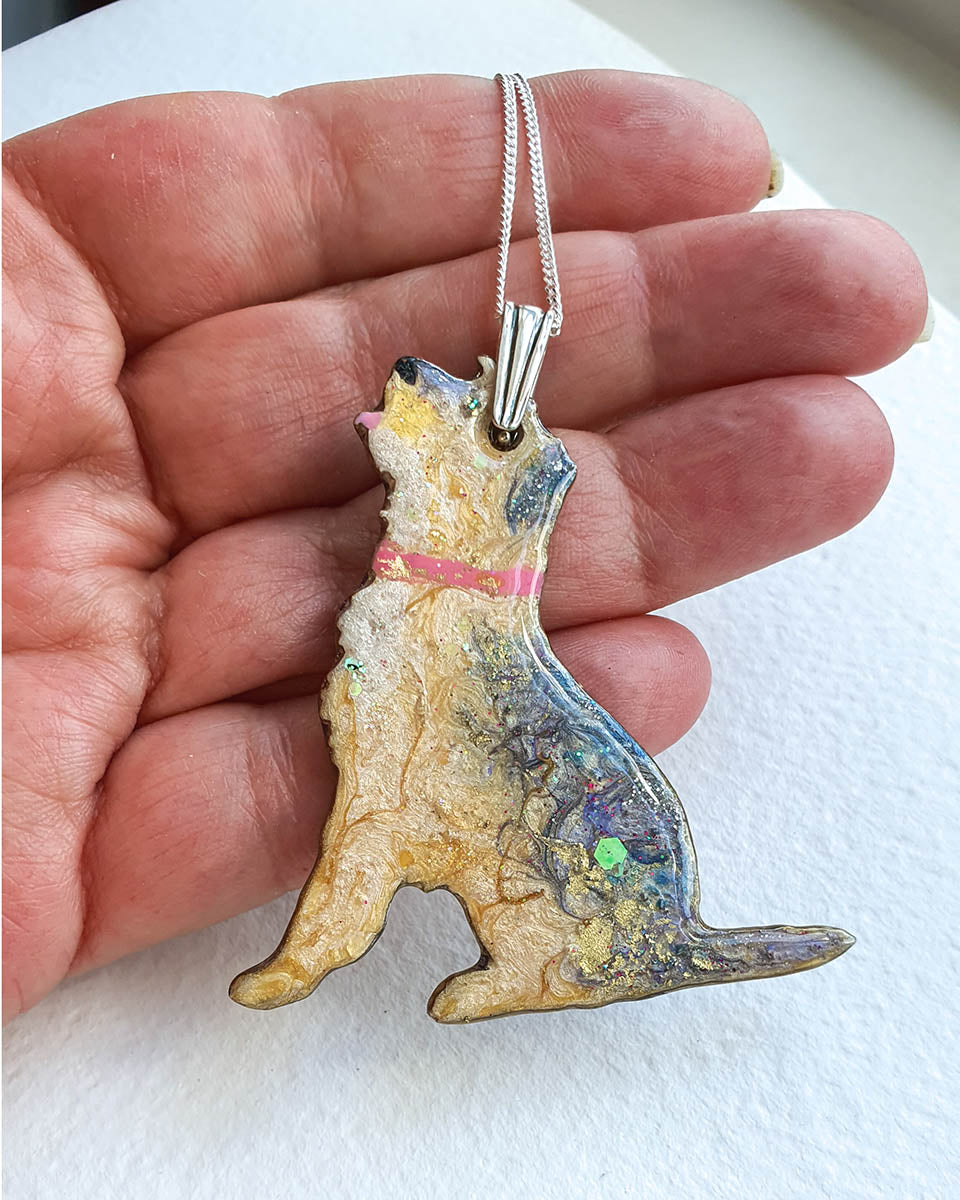 Border terrier dog shaped Blue and gold  pendant held in a hand against a white background