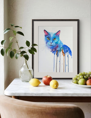 Framed watercolor painting of a colorful cat on a table with fruit and a plant.