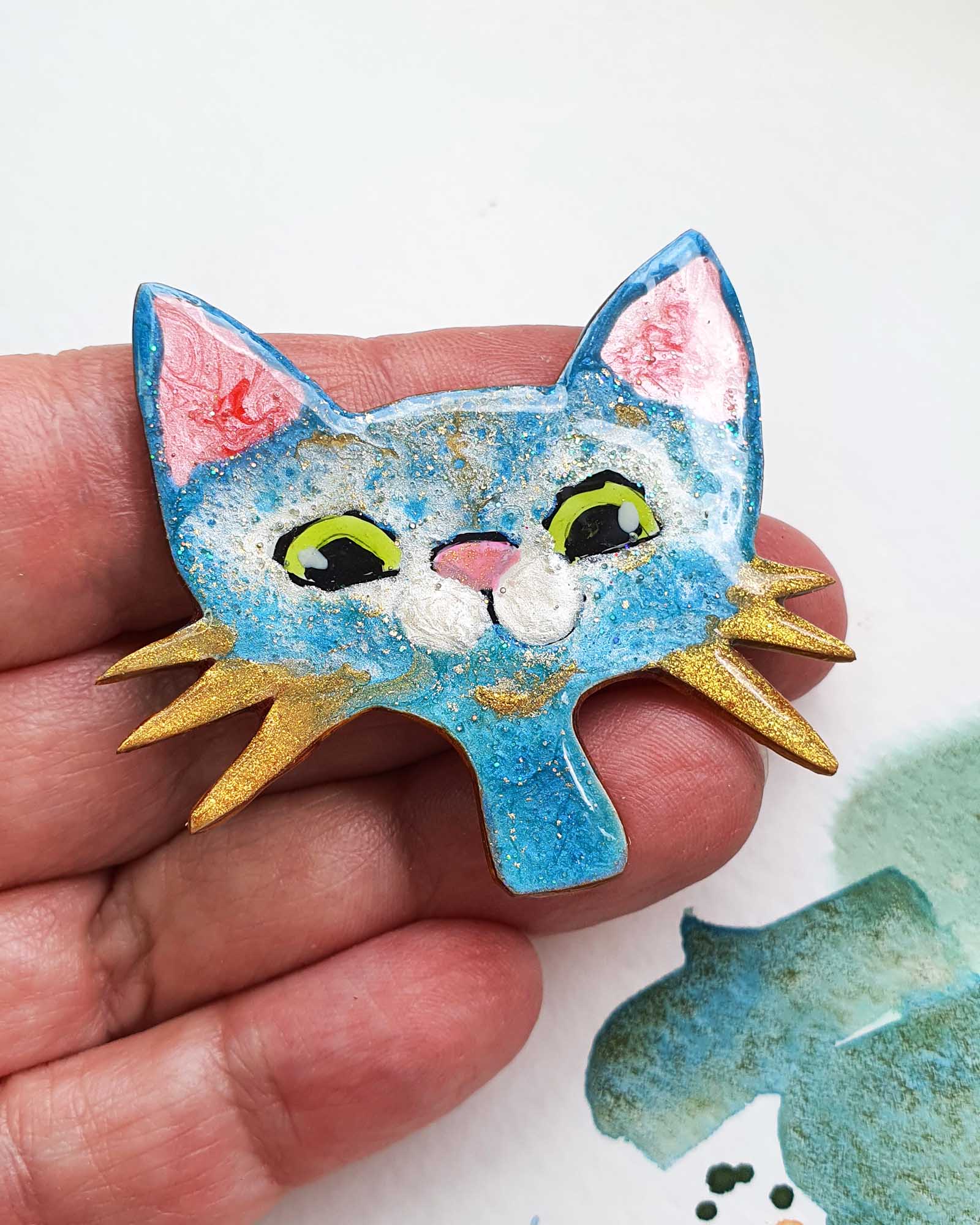 A unique handmade cat brooch from my catitude series.  She is a blue cat with green eyes, a cute pink nose and gold whiskers. A whimsical, fun cat face brooch.