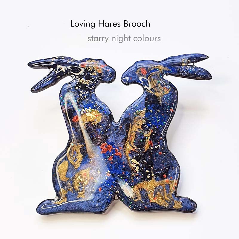 a pair of loving hares brooch, the are handmade in a starry night design, blues, blacks gold and they twinkle like a starry night.
