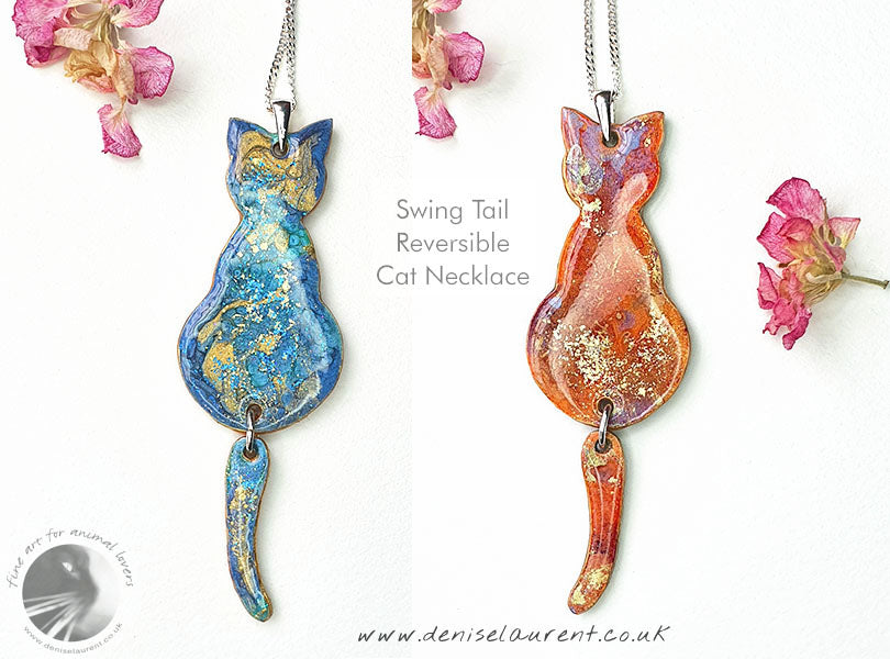 a handcrafted swing tail cat double sided necklace. these cats have free swinging tails, it blue and gold on one side and orange and gold on the other. A statement pendant for cat lovers.